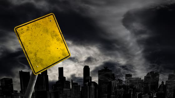 An image of a warning street sign in front of a city with hurricane weather approaching; image used for blog post about disaster fraud for not-for-profit