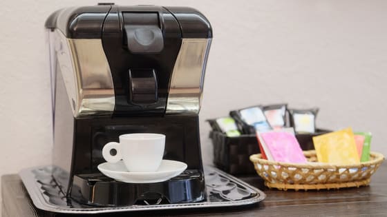 A photo of a coffee maker machine with a ceramic mug, sugar, and sweeteners sitting in a basket; image used for blog post about fringe benefits