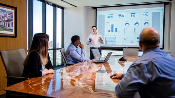 A photo of a team of professionals conducting a meeting with a presentation of analytics and data; image used for blog post about why companies should invest in a brand refresh