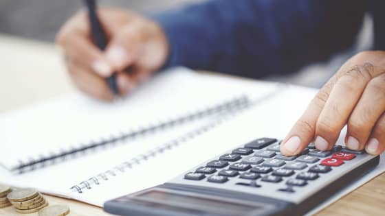 An image of someone typing on a calculator and writing on financial documents; image used for blog post about qualifying for QBI deductions