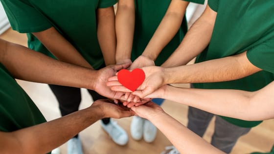 A photo of a team of people putting their hands together in a huddle with a paper heart in the middle; for blog post about not-for-profits passing public support test