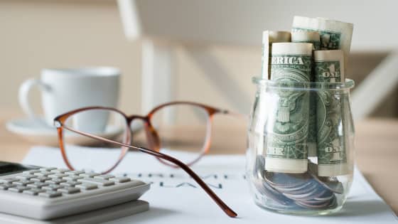 An image of a calculator, reading glasses and a jar of dollar bills sitting on a retirement plan document; for blog post about tax implications of retiring