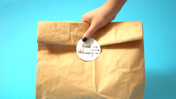 A photo of someone's hand grasping a paper back with a sticker that says "food delivery;" for blog post about gig worker economy tax consequences