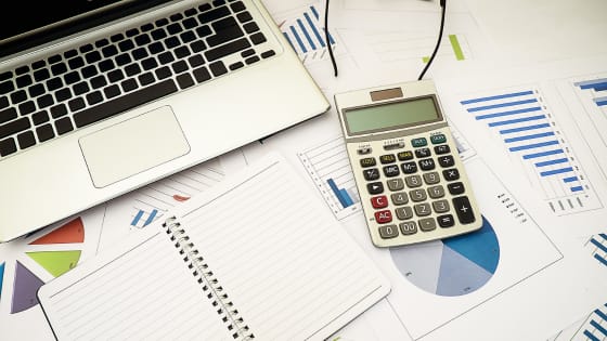 A photo of a calculator, journal, and laptop sitting on financial documents; for blog post about guaranteeing a loan for coporation