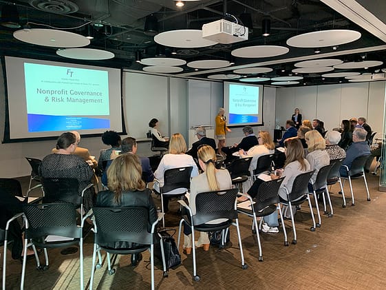 three rows of people sitting in chairs in an open room, facing towards two speakers and project screens for the seminar "nonprofit governance & risk management"