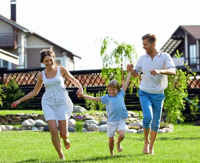 A family joyfully running across a green lawn exemplifying good lawn care and maintenance, with a home in the background