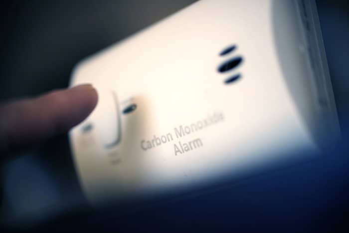 Close-up of a person pressing a button on a carbon monoxide alarm for testing