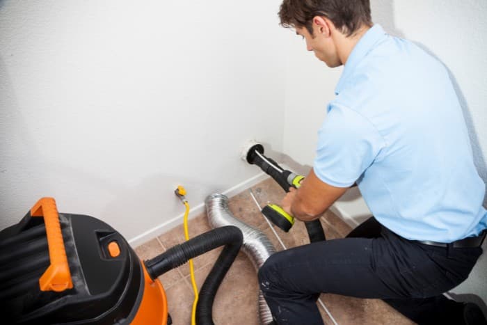 Technician performing dryer vent maintenance using a shop vacuum