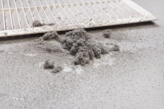 a pile of dust and debris on a surface, with a dirty air filter in the background