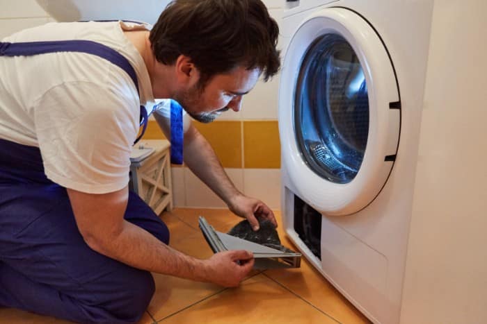 Technician performing maintenance by clearing lint from a dryer’s lint trap