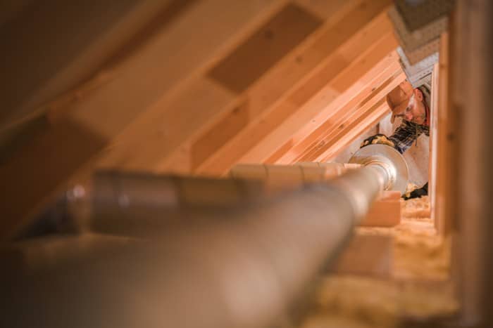 a professional technician working in an attic, focusing on an air duct system