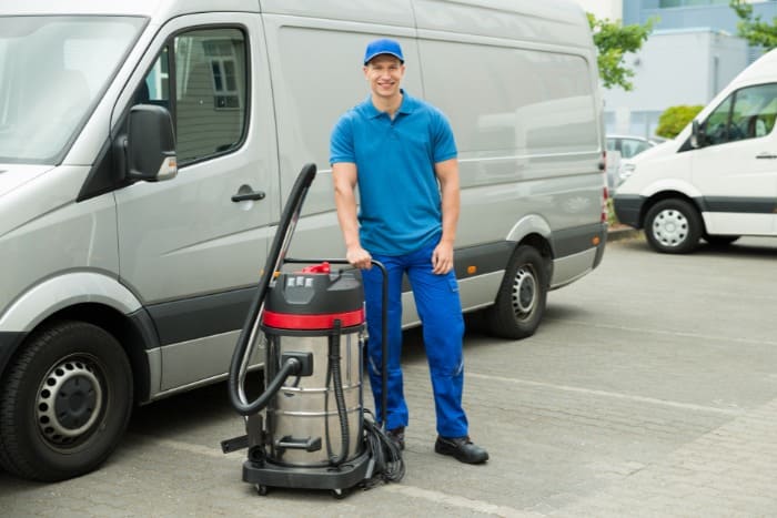 Professional vent cleaner standing beside a shop vacuum and service van