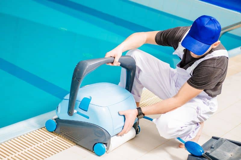 man with a pool vacuum near a swimming pool