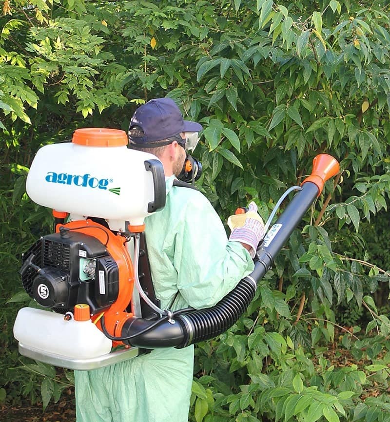 pest control professional wearing protective gear and using an "agrofog" fogging machine to spray plants